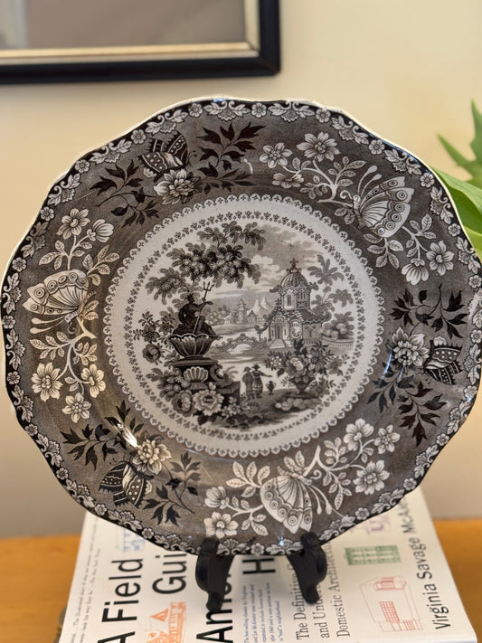 Decorative plate with intricate black and white floral and landscape design on a stand.
