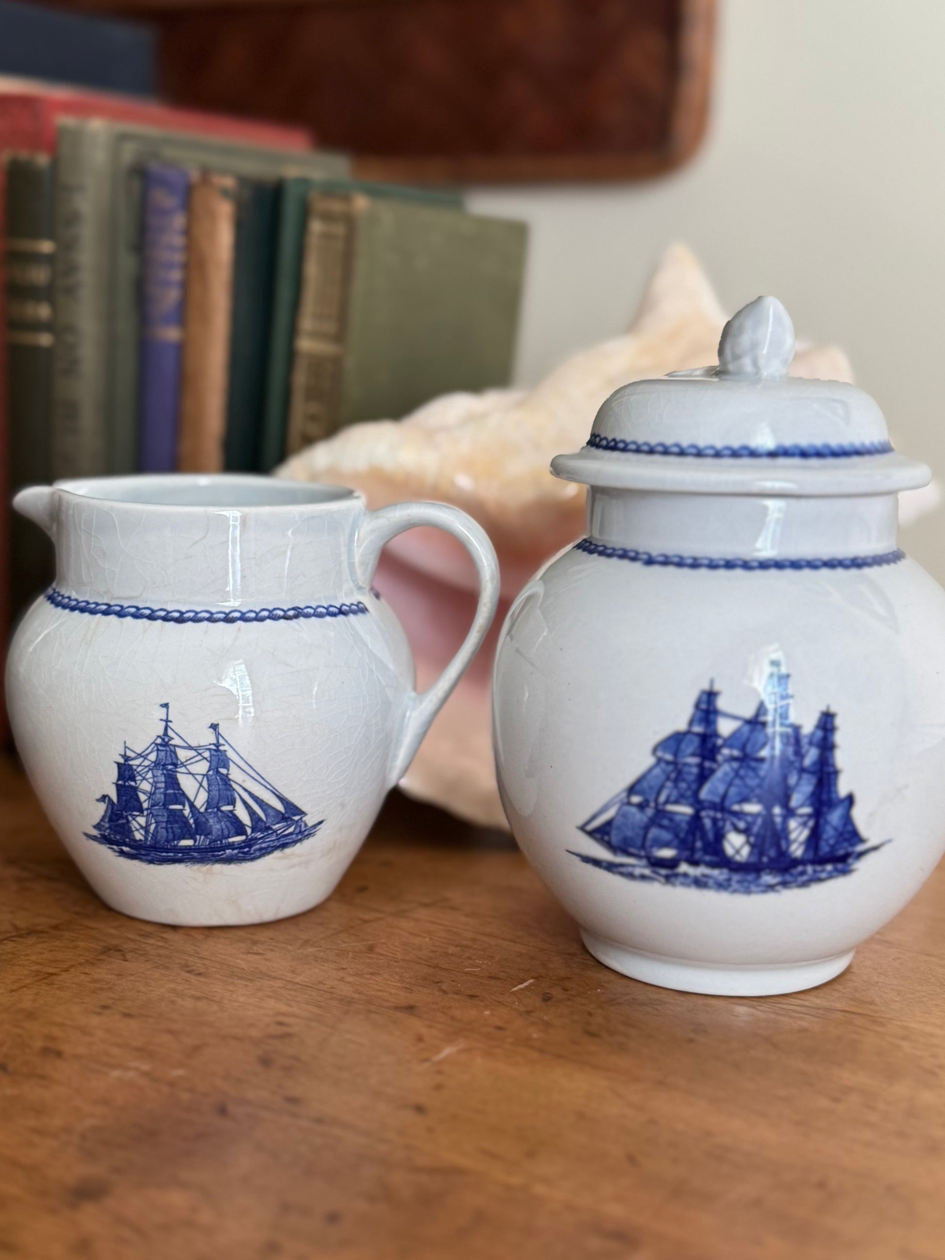 White with blue ship creamer and sugar bowl set on wooden surface
