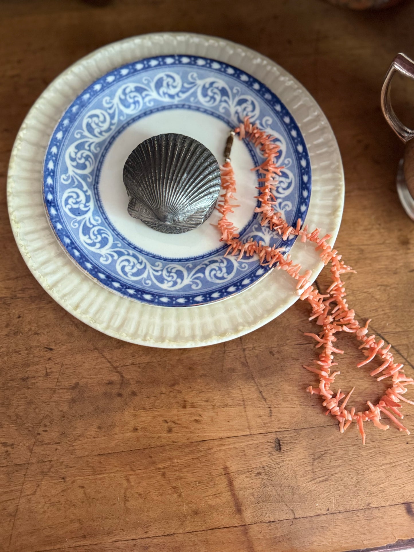 Decorative plate with blue and white pattern featuring a shell and coral on a wooden surface