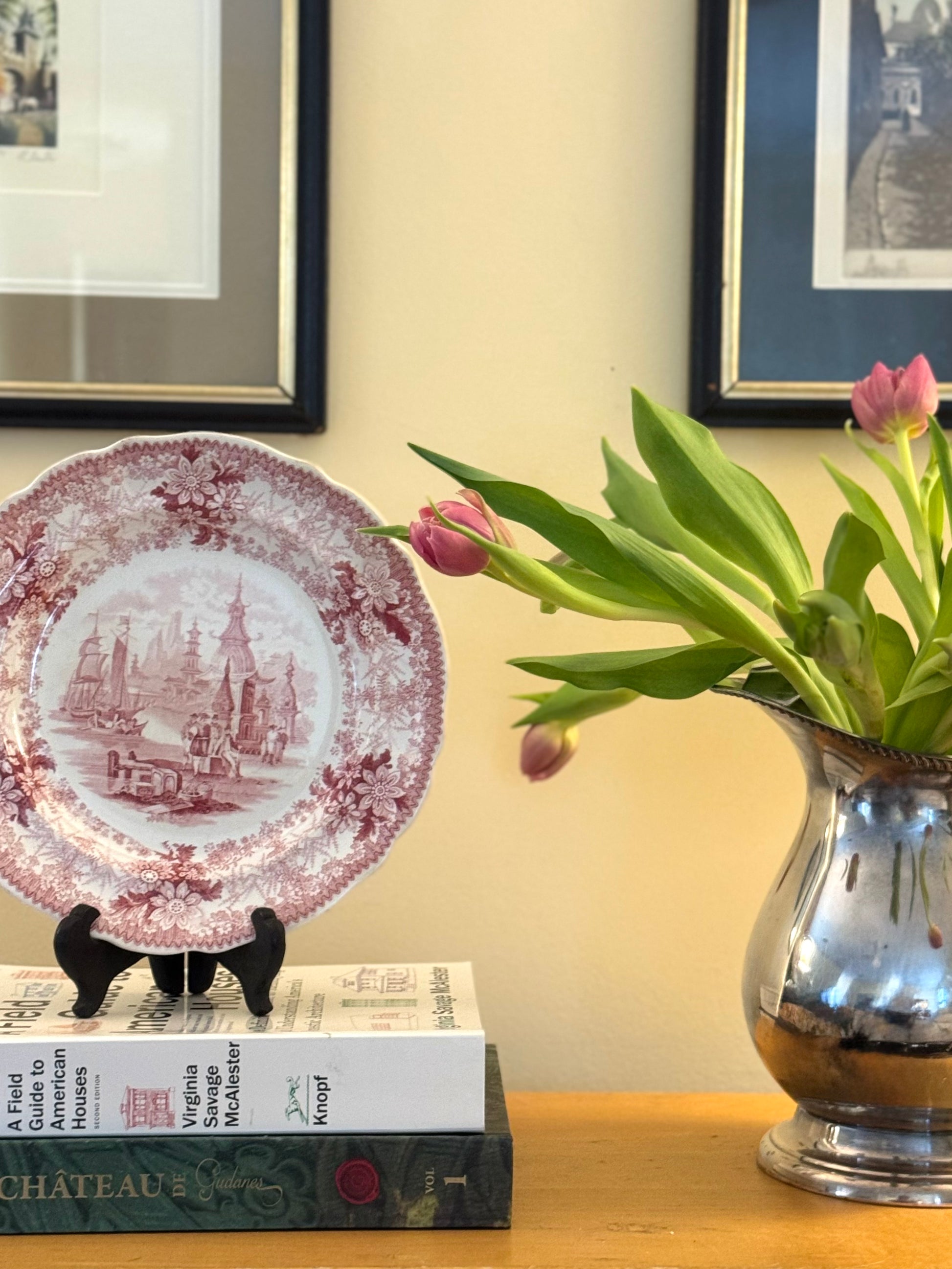 Decorative plate with a floral design, books, and a vase with flowers on a table.