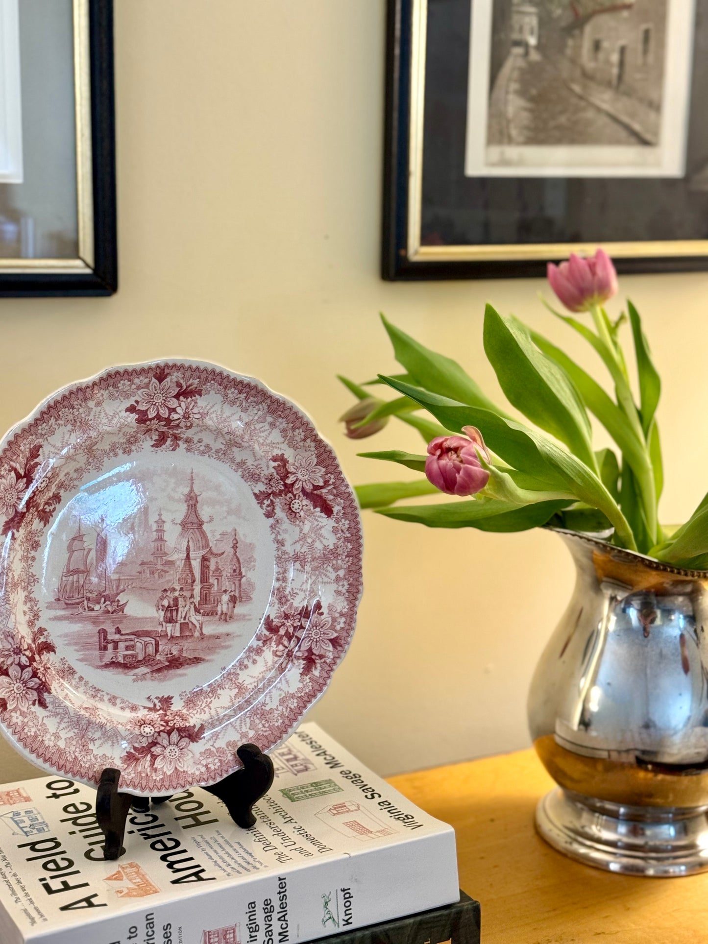 Decorative plate with a castle design on a stand next to a vase with tulips on a table.