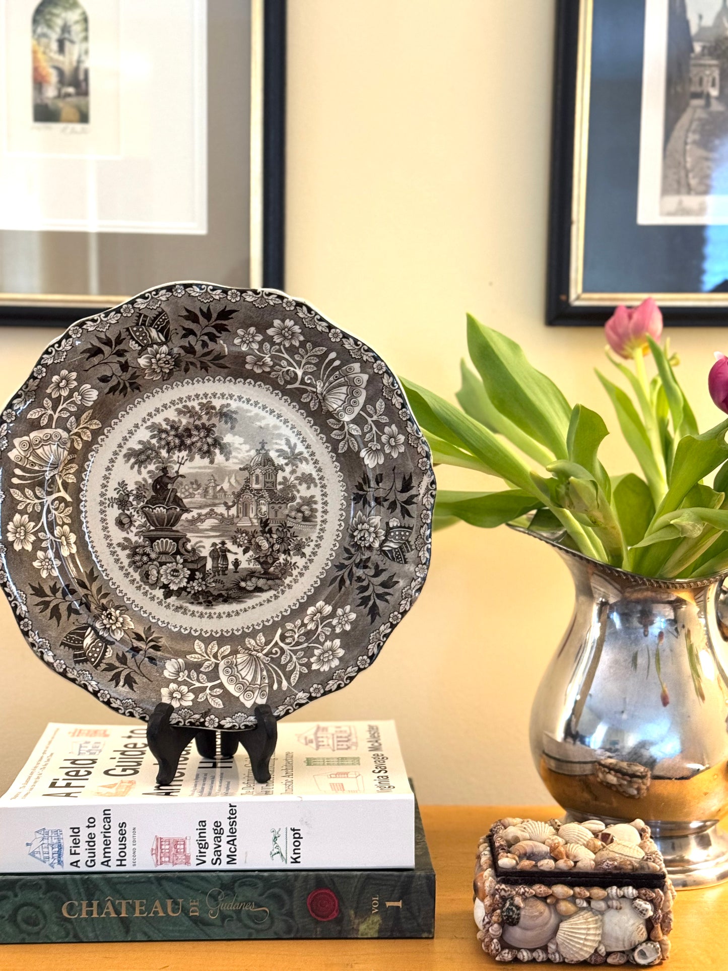 Decorative plate on books with a vase of tulips in the background