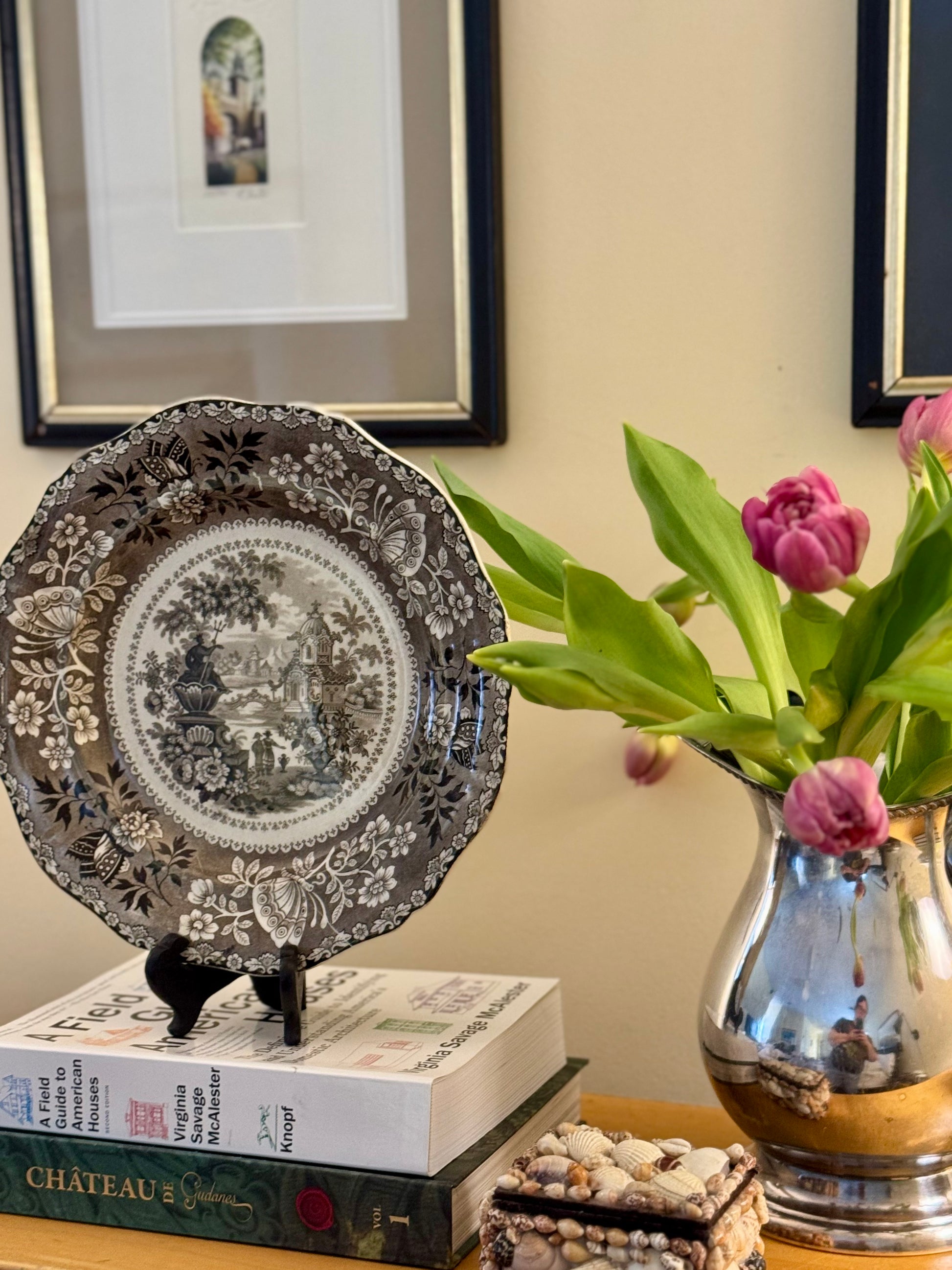 Decorative plate on books with a vase of flowers in the background