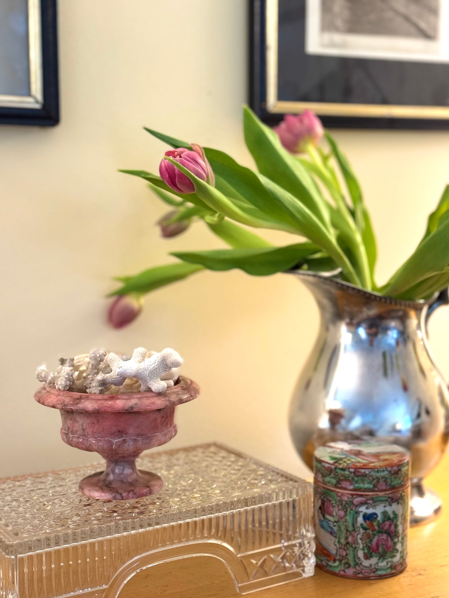 Decorative items including a pink urn, silver vase, and floral arrangement on a table.