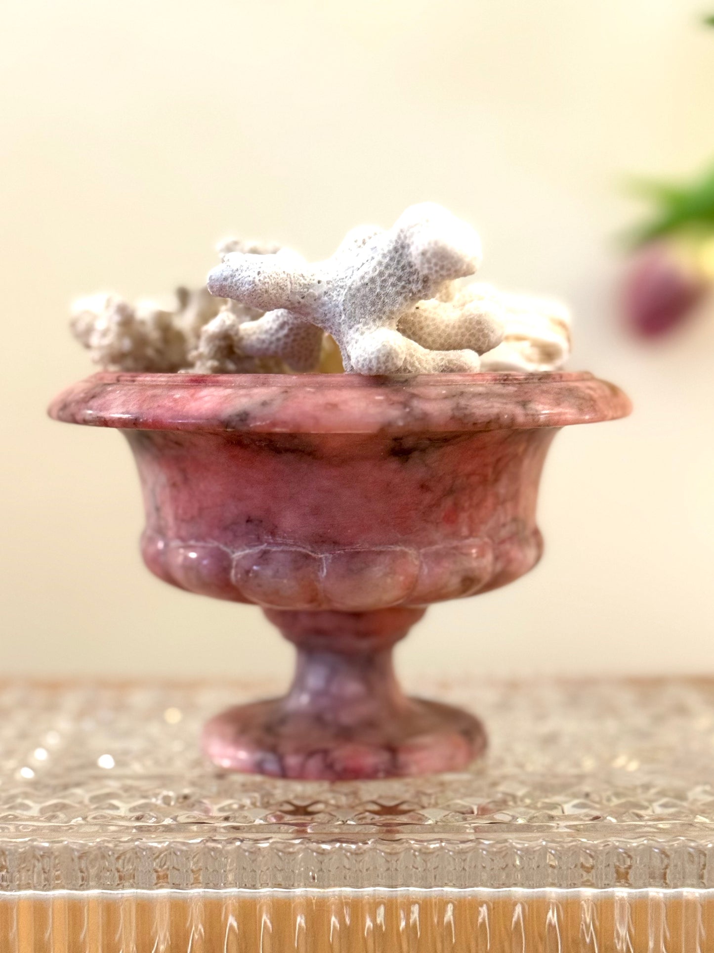 Decorative pink marble bowl with coral on a beige surface